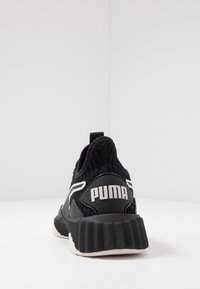 Černá atletická bota s pleteným svrškem, která má bílé akcenty, silnou texturovanou podrážku a výrazné logo "PUMA" na patě.