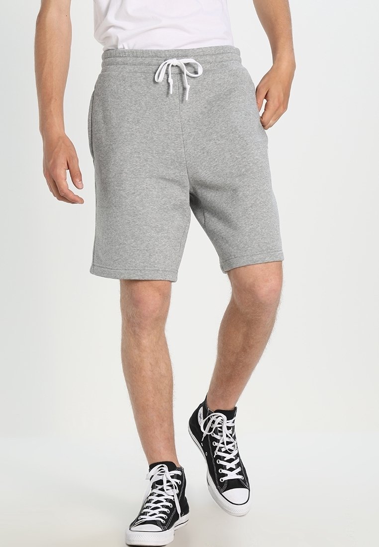 Shorts gris en mélange de coton avec une taille élastique et un cordon de serrage. Bords ourlés et poches latérales. Associés à des baskets en toile noires.