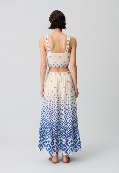 Conjunto de dos piezas que incluye un top corto crema con patrones florales azules y una falda larga en un diseño en degradado azul con motivos geométricos.