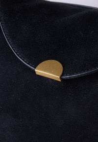 Black suede wallet with curved flap secured by a semicircular brass clasp in close-up view.