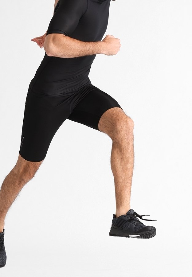 Bodysuit atlético negro con mangas cortas y pantalones cortos ajustados. Combinado con zapatillas negras texturizadas, demostrando movimiento.
