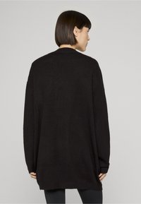 Prevelik črn pleten pulover z mehko teksturo in rebrastimi manšetami, z okroglim izrezom in daljšo zadnjo stranjo.