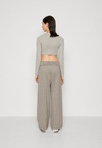 Sivý crop top s dlhým rukávom v kombinácii s pohodlnými nohavicami so širokými nohavicami a károvaným vzorom, ktoré majú gumičkový pás, z pohľadu zozadu.
