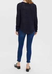 Pullover in maglia navy con pattern testurizzato, colletto rotondo e orlo curvo, abbinato a jeans skinny blu e scarpe con tacco blocco nere.