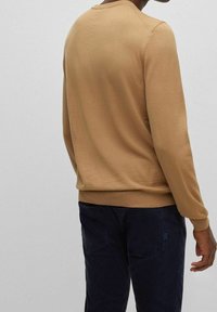 Maglione beige a maglia con scollo rotondo, polsini e orlo aderenti; abbinato a pantaloni navy con tasche posteriori e dettagli di texture.