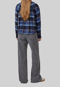 Karierter blau-schwarzer Flanellhemd mit langen Ärmeln, kombiniert mit lockerer grauer Jeans und hellen Schuhen.