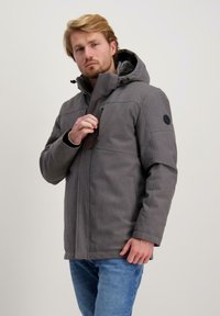 Grijze geïsoleerde jas met een capuchon, ritssluiting aan de voorkant en zijzakken. Beschikt over een gestructureerde stof en een zwart rond logo op de mouw.