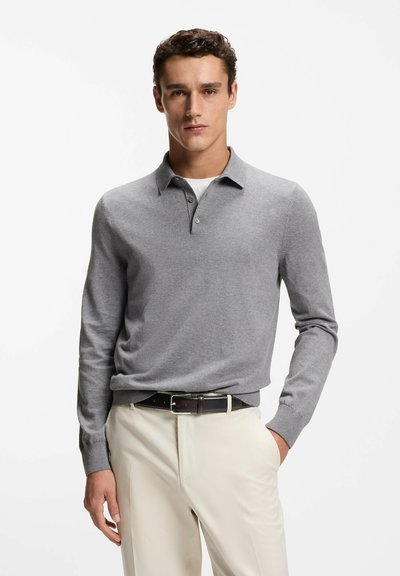 Polo gris de manga larga hecho de tela suave, con cuello, tres botones y puños acanalados, combinado con pantalones beige claro.