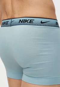 Γαλάζια ανδρικά εσώρουχα μπόξερ με ζώνη μέσης με μοτίβο σε μπλε χρώμα που φέρει μαύρα λογότυπα Nike, φορεμένα από αρσενικό μοντέλο που παρουσιάζεται από πίσω.