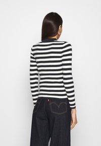 Pull côtelé rayé noir et blanc à manches longues, coupe ajustée, col rond, associé à un jean en denim foncé avec des coutures contrastantes.