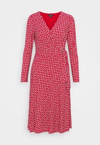 Czerwona sukienka wrap z długimi rękawami, zdobiona geometrycznym białym i czarnym wzorem, wykonana z gładkiego materiału, wysmuklona w talii za pomocą wiązania.