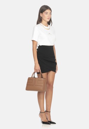 T-shirt bianco, gonna avvolgente nera e décolleté nere a punta. Borsa marrone con texture e due tasche frontali.