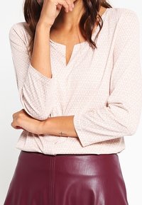 Lichtroze blouse met een subtiele bloemenpatroon, driekwartmouwen en een uitsnijding in de hals, gecombineerd met een bordeauxleren rok.