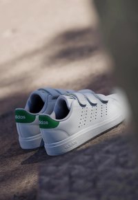 Baskets blanches de sport avec des accents verts, dotées d'une tige en synthétique lisse, de languettes en velcro et de détails perforés sur les côtés.