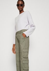 Light lavender sweater with long sleeves paired with olive green cargo pants featuring multiple pockets and a relaxed fit.
