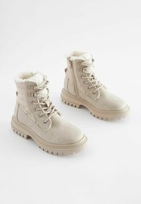Beige enkellaarsjes van glad leer met een gestructureerde bontvoering, vetersluiting aan de voorkant, enkelhoogte en een robuuste zool voor grip.