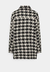 Mantel im Hahnentrittmuster in Schwarz und Creme, mit Kragen und langen Ärmeln, aus strukturierter Stoff gefertigt, zeigt eine Rückansicht.