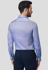 Jasnoniebieska koszula z długim rękawem, wykonana z gładkiego materiału, z klasycznym kołnierzykiem i guzikami, widoczna z tyłu.