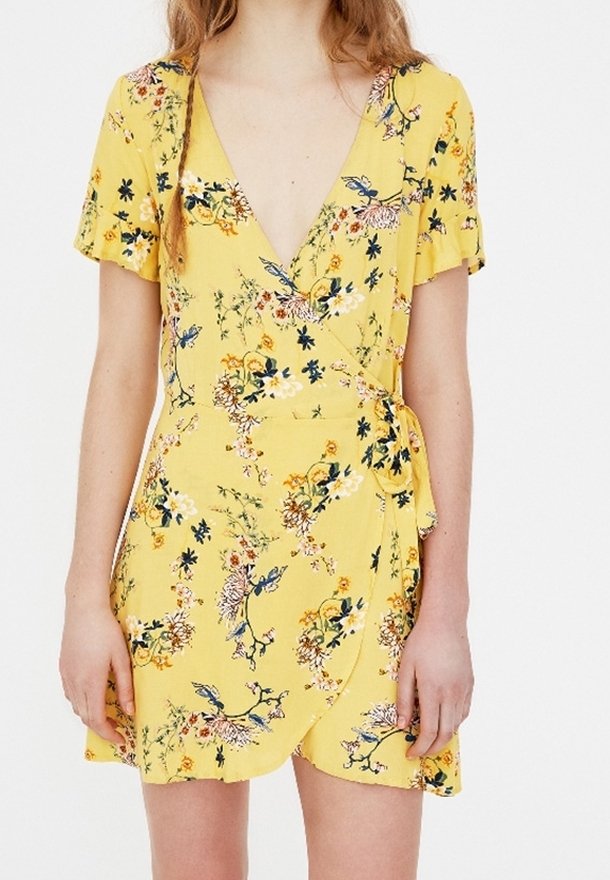 Robe portefeuille jaune avec manches courtes à volants, imprimé floral multicolore, décolleté en V profond et fermeture à nouer sur le côté gauche.