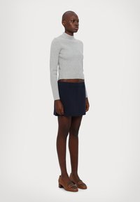 Pulover turtleneck ribbed de culoare gri deschis și fustă șort navy, asortate cu pantofi cu toc pătrat maro. Texturi netede și design ajustat.