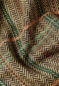 Houndstooth-mönstrad tyg i guld, svart, grön och orange nyanser. Mjuk textur med en vävd design med zigzaglinjer i olika färger.