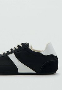 Deportiva en blanco y negro con parte superior de lona, cordones planos, detalles blancos y suela texturizada para agarre y durabilidad.