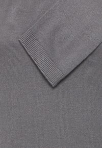 Gros plan d'une manche en tissu tricoté gris avec un détail de poignet côtelé sur un fond tricoté gris assorti.