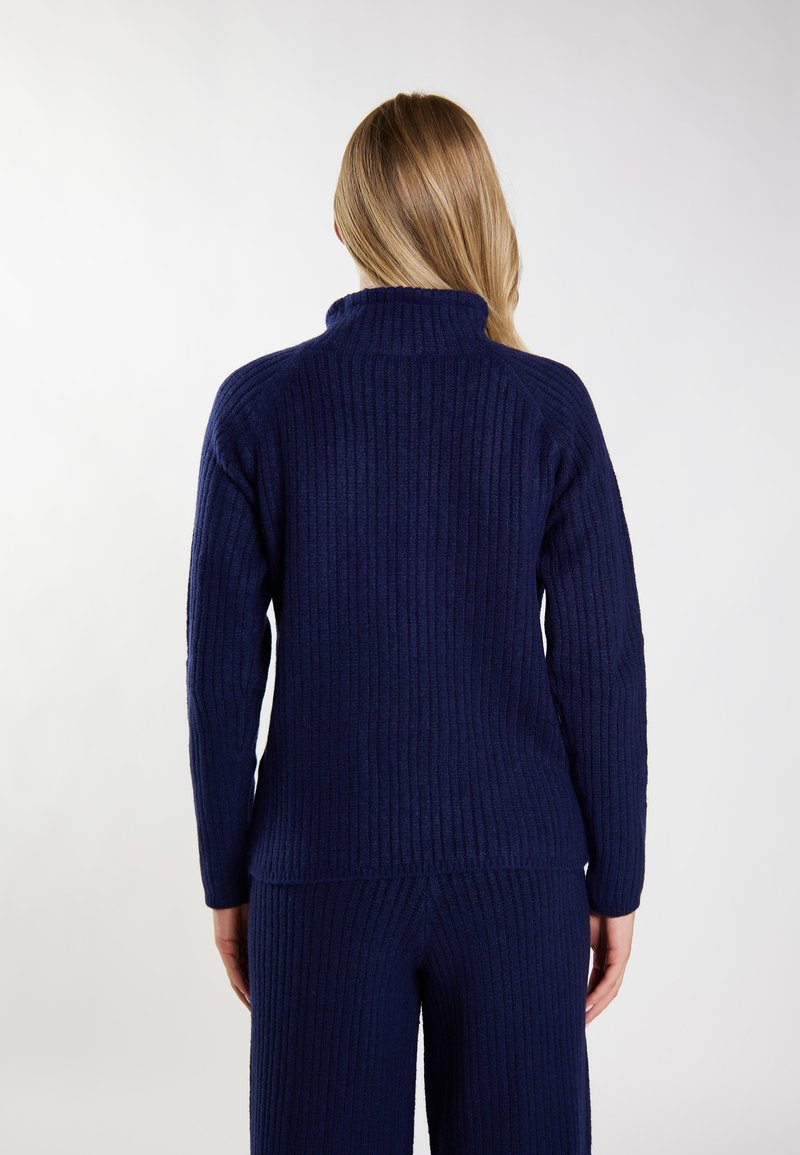 Maglione a coste blu navy con colletto alto e maniche lunghe, caratterizzato da un motivo a maglia testurizzato. Mostrato da dietro, abbinato a pantaloni coordinati.
