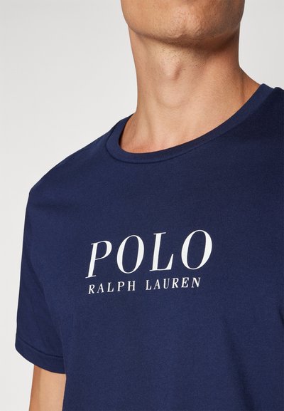 Sötétkék pamut póló, rövid ujjakkal és kerek nyakkivágással, fehér "POLO RALPH LAUREN" logóval a mellrészen.