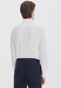 Biała długa koszula z klasycznym kołnierzykiem, listwą guzikową i subtelną fakturą. Połączona z granatowymi spodniami z tylnymi kieszeniami.