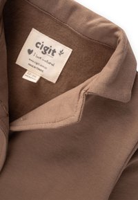 Colletto di camicia in cotone marrone con una texture morbida. Contiene un'etichetta in tessuto con il marchio "cigit", taglia 12-18 mesi e nota di materiale naturale.