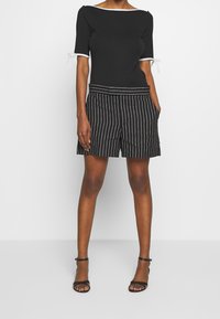 Černé tričko s bílým lemem a krátkými rukávy doplněné černobílými pruhovanými šortkami. Šortky mají kapsy a uvolněný střih.