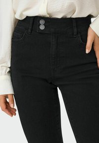 Vaqueros de mezclilla negros de tiro alto con una textura suave, que cuentan con dos botones plateados, bolsillos laterales y costuras tonales.
