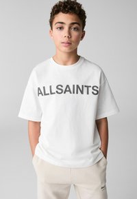 Vit bomullströja med "ALLSAINTS" tryckt i fet svart text. Rund hals, korta ärmar och avslappnad passform. Passar bra med ljusa byxor.