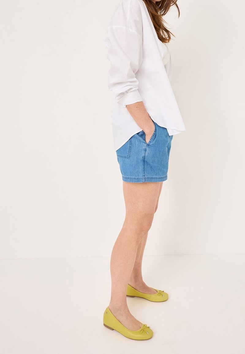 Lichtblauwe denim shorts met zijzakken, gecombineerd met een wit langslouch shirt en gele balletflatjes met strikaccenten.