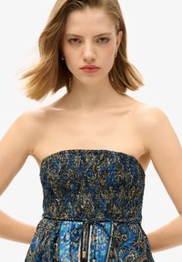 Robe sans bretelles avec un haut smocké, ornée de motifs paisley intricats bleu, noir et or ; lien ajustable à la taille.