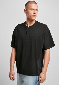 Svart kortermet henley-skjorte laget av bomull, med en tre-knaps placket og avslappet passform, kombinert med lyseblå jeans.