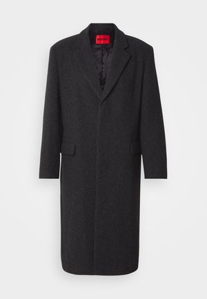 Abrigo de mezcla de lana negra con una silueta ajustada, solapas de muesca, dos bolsillos frontales y un forro interior brillante. Etiqueta de la marca visible.