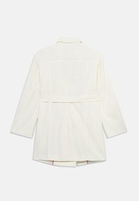 Λευκό παλτό τύπου trench με μακριά μανίκια, ζώνη στην πλάτη και κεντρική πιέτα, σε απλό λευκό φόντο.