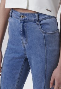 Jeans de denim azul de cintura alta que presentan un diseño clásico de cinco bolsillos, un ligero desgastado y un cierre frontal de botón metálico.