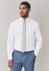 Camicia bianca, cravatta beige a motivi con fermacravatta e pantaloni azzurri. Tessuto liscio con vestibilità su misura.