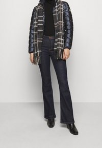 Topattu tummansininen hupullinen takki, musta pooloneule, ruudullinen huivi, tummat väljälahkeiset farkut ja mustat nilkkurit.