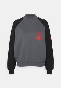 Grå sweatshirt med svarta raglanärmar, hög krage, ribbade mudd och nederkant. Har röd "Quiksilver" logotyp och patchdetalj på ärmen.