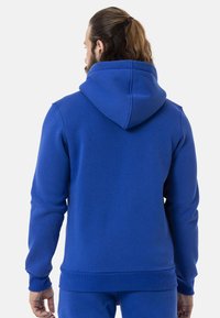 Blauer Hoodie mit großer Kapuze, gerippten Bündchen und Saum. Der Stoff wirkt weich und strukturiert und zeigt ein einfaches, einfarbiges Design.