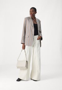 Stripet blazer i lyse toner med lange ermer, kombinert med en svart topp og vide hvite bukser. Holder en beige strukturert håndveske.