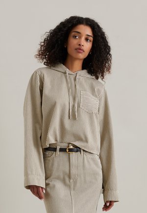 Striped beige hoodie featuring a front pocket, drawstring hood, and loose fit, paired with matching striped skirt and black belt.