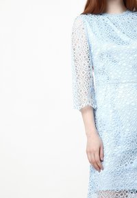 Ljusblå spetsklänning med ett strukturerat, cirkulärt mönster och trekvartsärmar; har scallopade kanter och en figurnära midja.