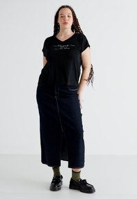 Μαύρο cropped t-shirt με κείμενο, σκούρα τζιν μάξι φούστα με μπροστινό σκίσιμο, σκούρα παπούτσια και πράσινες κάλτσες. Λείο ύφασμα και άνετη εφαρμογή.