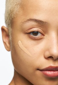 Fondation appliquée sur une peau claire. Texture lisse, fini naturel. Gros plan du visage montrant le teint de la peau et la consistance du produit sur la peau.