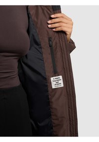 Brown puffy jacket interior showcasing a smooth, dark lining with a black zipper and a label reading, "A warm hug made out of cloth."
